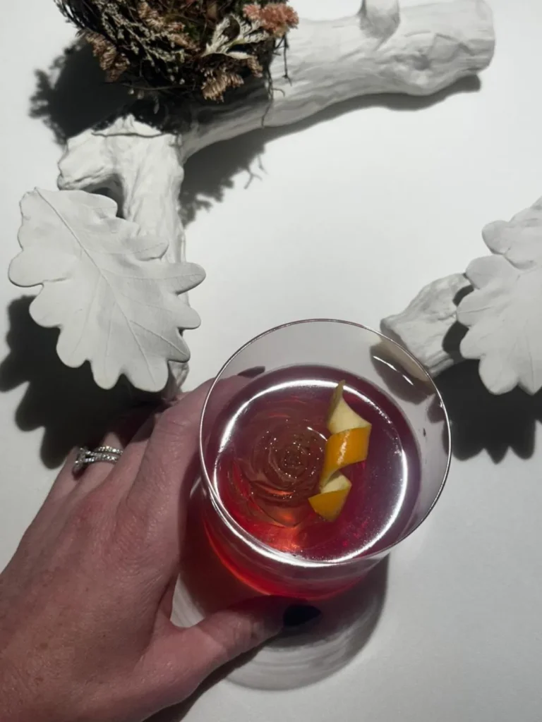 Mano de mujer con anillo de compromiso sosteniendo un Negroni. Luna de miel en Sudáfrica.